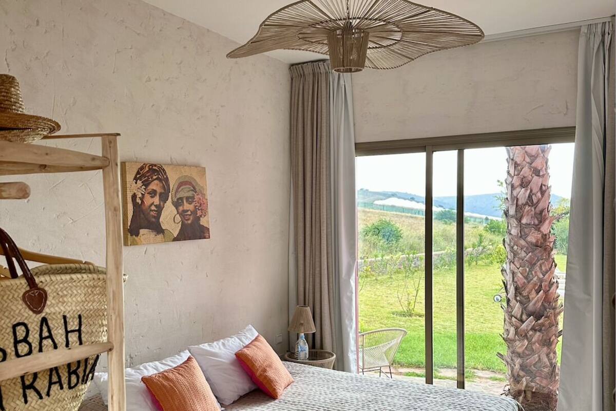 Un dormitorio con una cama grande, un lámpara colgante, vistas al exterior y una cesta fijada a la pared con texto.