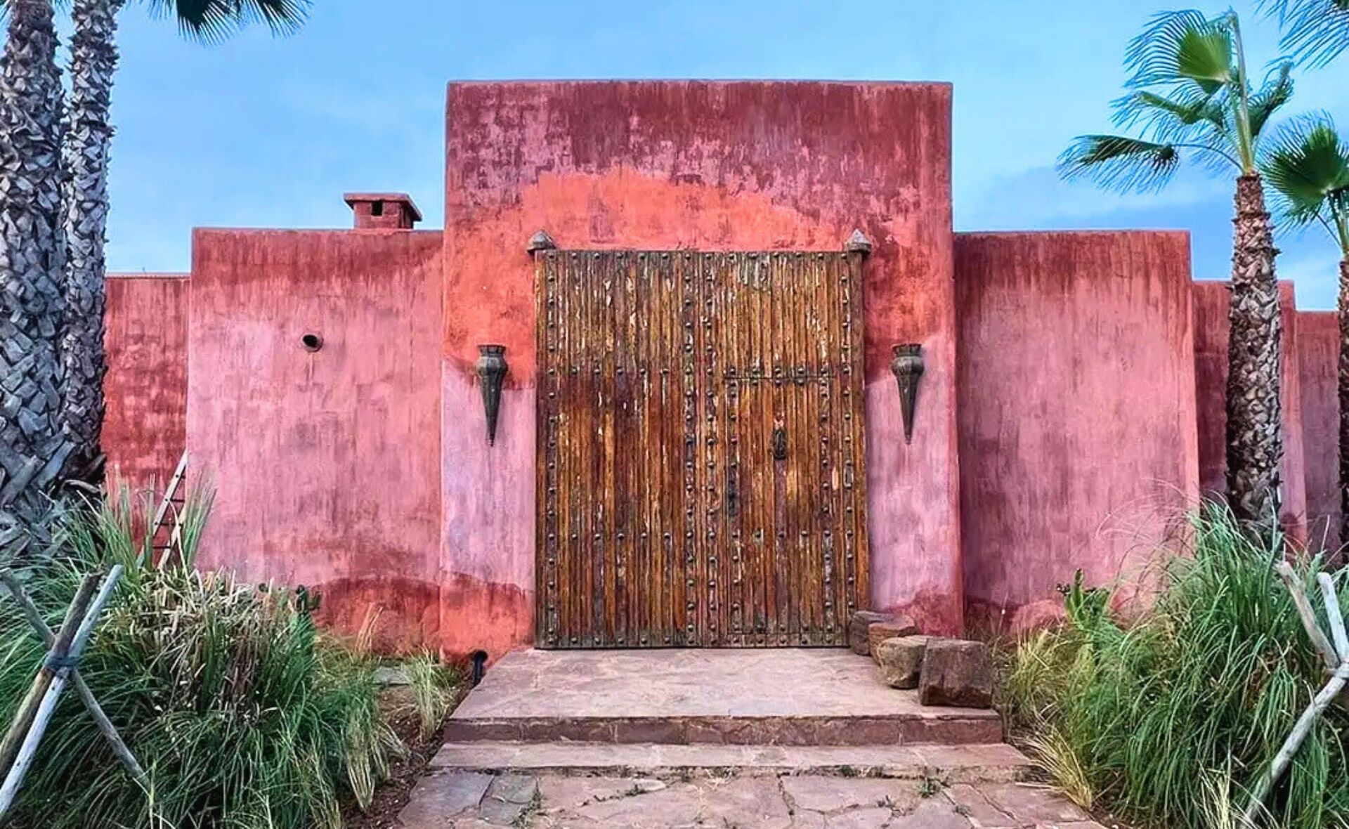Un edificio de paredes rojas con un portón de madera y escalones que conducen a la entrada.