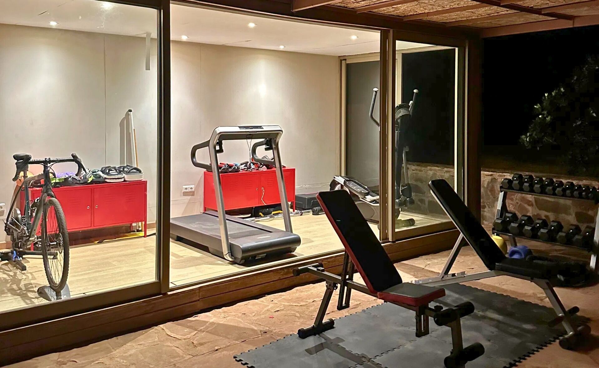 Un gimnasio en casa con cinta de correr, bicicleta estática y banco para pesas.