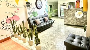 A lobby with a sofa, potted plants, a clock, and a reception desk.