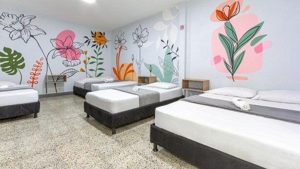 Habitación de hotel con cuatro camas individuales, un kitchenette y una pared decorada con coloridos murales florales.