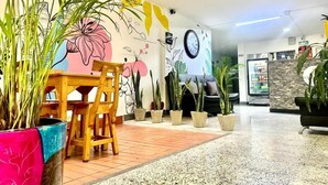 Un vestíbulo amplio con una mesa y sillas de madera, plantas en macetas y un mural colorido en la pared.
