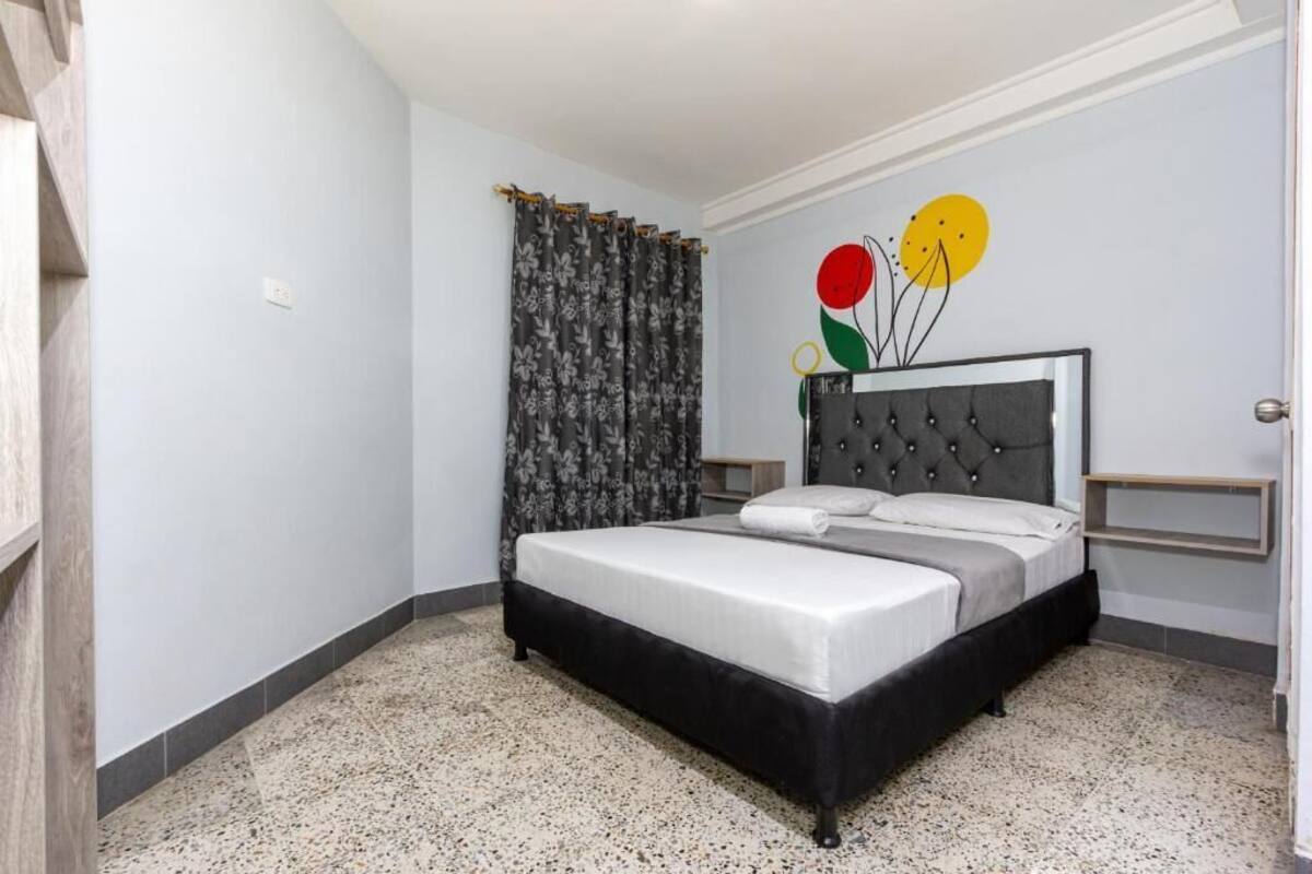 Un dormitorio con cama, cortinas, una obra de arte en la pared y una mesita de noche.