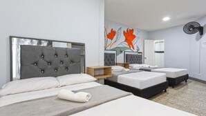 A hotel room with a large bed, two smaller beds, a mirror, and a wall with a floral mural.