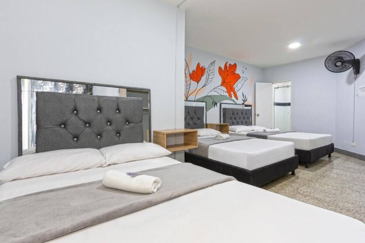 Habitación de hotel con una cama grande, dos camas más pequeñas, un espejo y una pared con un mural floral.