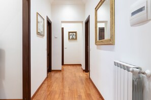 A hallway with wooden flooring, white walls, and framed pictures. There is a radiator on the right wall and a door at the end of the hallway. - Elegant Salandra Suite (Rome)