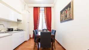 A compact kitchen with white cabinets, a dining table with four chairs, and a painting on the wall. - Elegant Salandra Suite (Rome)