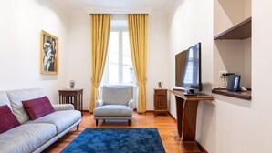 A living room with a sofa, armchair, TV, and wooden sideboard. - Elegant Salandra Suite (Rome)
