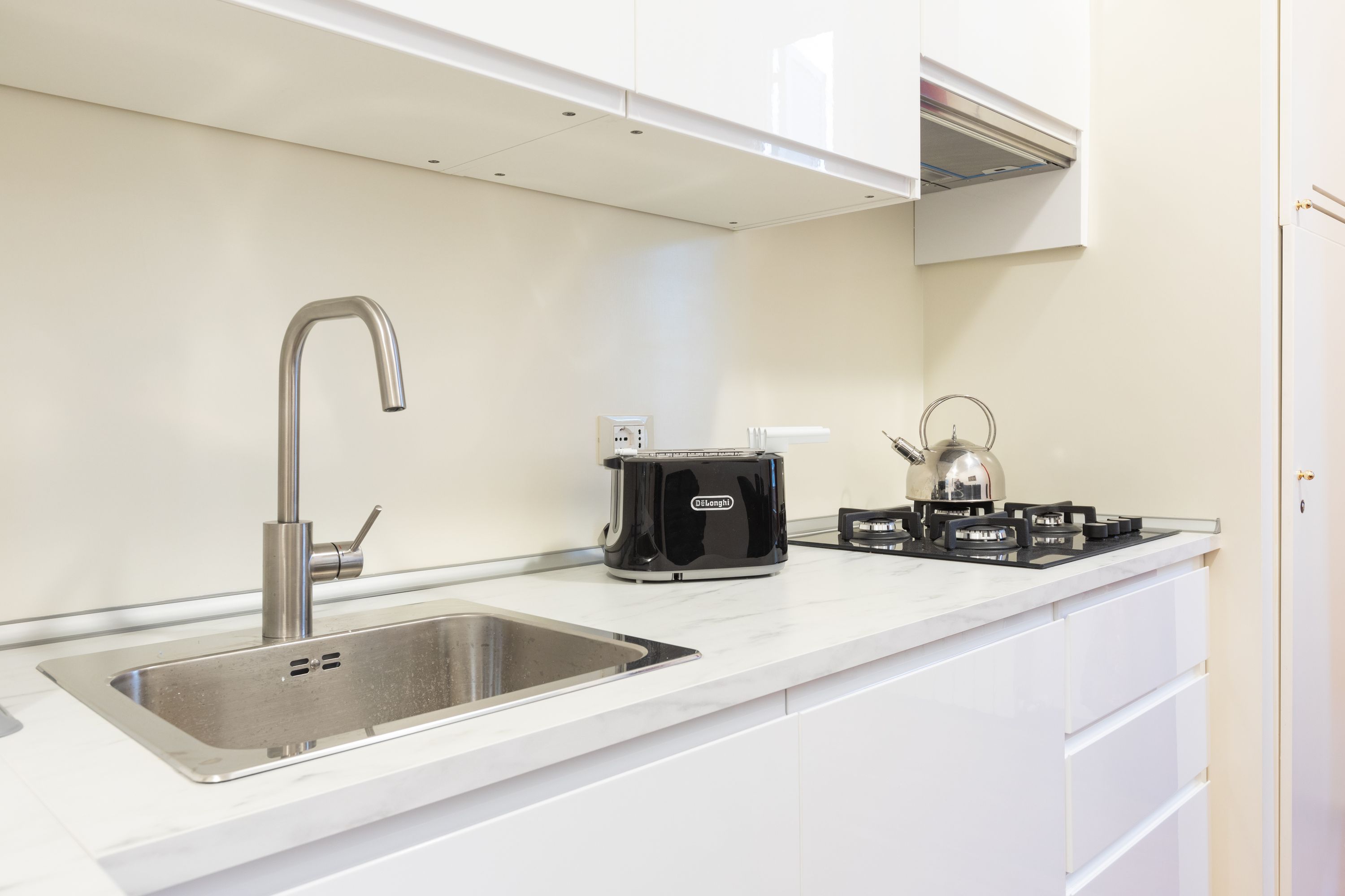 Una cocina moderna con un lavamanos de acero inoxidable, una tetera eléctrica negra y una estufa a gas.