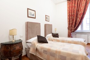 A hotel room with two beds, a wooden nightstand with a lamp, and a window with curtains. - Elegant Salandra Suite (Rome)