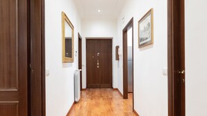 A hallway with wooden floors, a double door at the end, and framed pictures on the walls. - Elegant Salandra Suite (Rome)