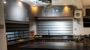 A modern kitchen with dark cabinetry, a central island with bar stools, and a pendant light. - Fully Furnished Two Bedrooms, Modern Kitchen, Wifi (Kumasi)