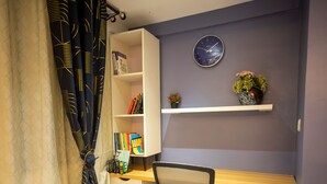 A room with a bookshelf, a clock, and a potted plant on a shelf. - Fully Furnished Two Bedrooms, Modern Kitchen, Wifi (Kumasi)