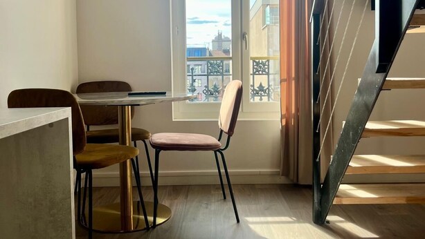 Een modern appartement met een eethoek, een trap en een groot raam met uitzicht op gebouwen.