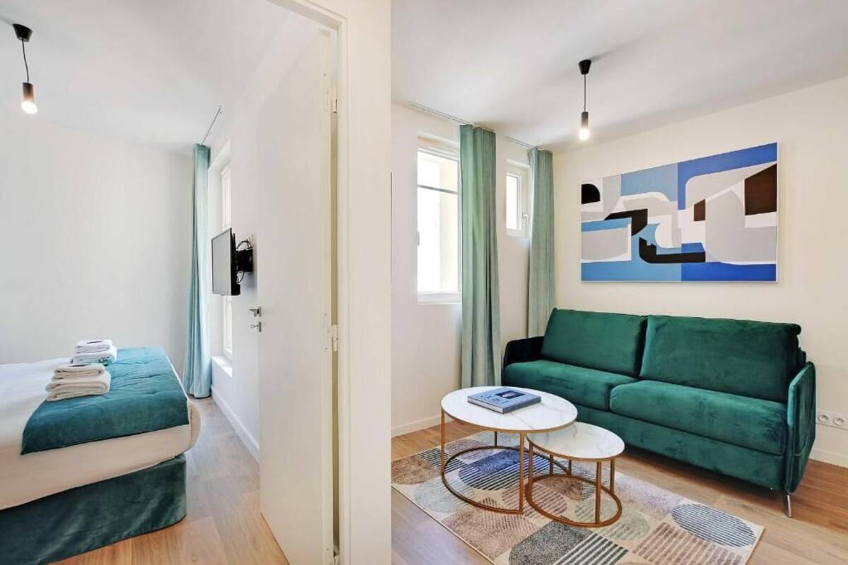 Una stanza moderna con un letto, un divano verde, un tavolino rotondo e un grande quadro astratto appeso alla parete.