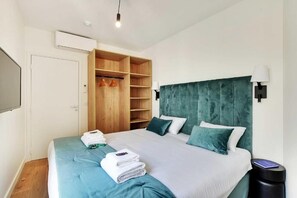 A hotel room with a bed, a wardrobe, a TV, and a trash bin. - La Lumière de Paris (Levallois-Perret)