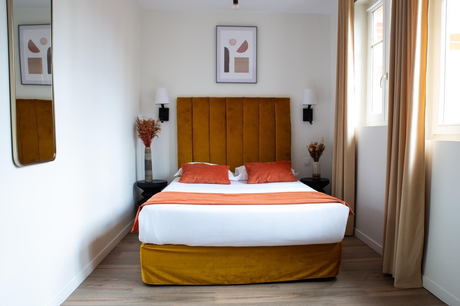 A hotel room with a large bed, two bedside tables with lamps, a headboard, and framed artwork on the walls.