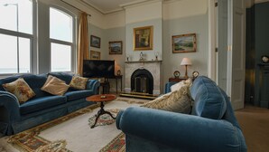 A living room with a blue sofa, a fireplace, and a television. - Edwardian Beach Villa in Whitehead, Beach Front Period Edwardian Villa (Whitehead)