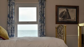 A bedroom with a large bed, a window with curtains, a framed picture on the wall, and a wooden headboard. - Edwardian Beach Villa in Whitehead, Beach Front Period Edwardian Villa (Whitehead)
