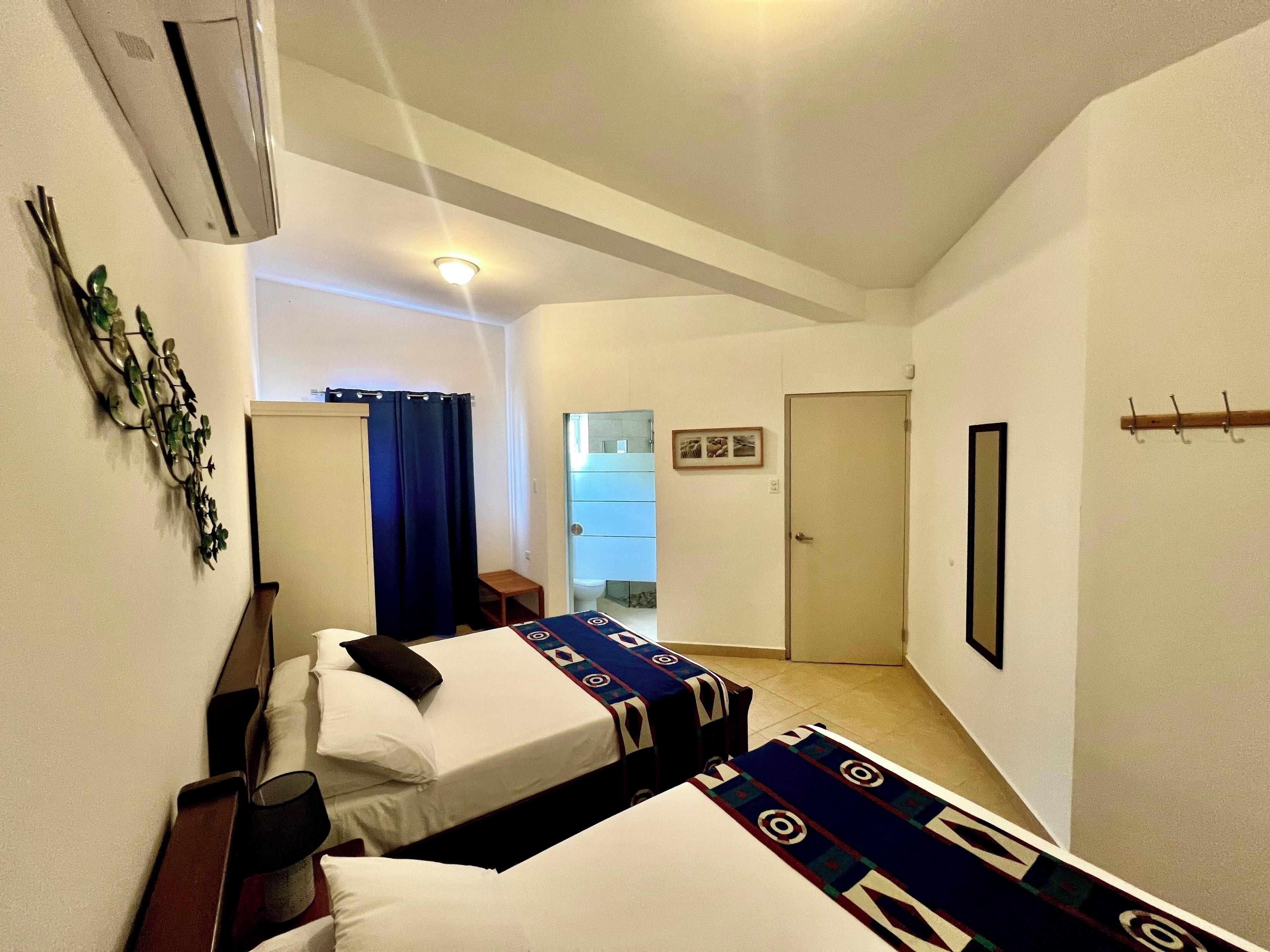 A hotel room with two beds, a shower area, and a door leading to a bathroom.