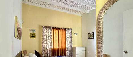 A hotel room with a bed, a nightstand, a lamp, a mirror, and a door.