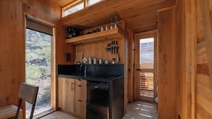 Cocina compacta con armarios de madera, encimera negra y lavavajillas integrado. Una ventana ofrece vistas al exterior.