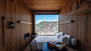 Un dormitorio de cabaña de madera con una ventana grande, una cama, una mesita de noche y un farol.