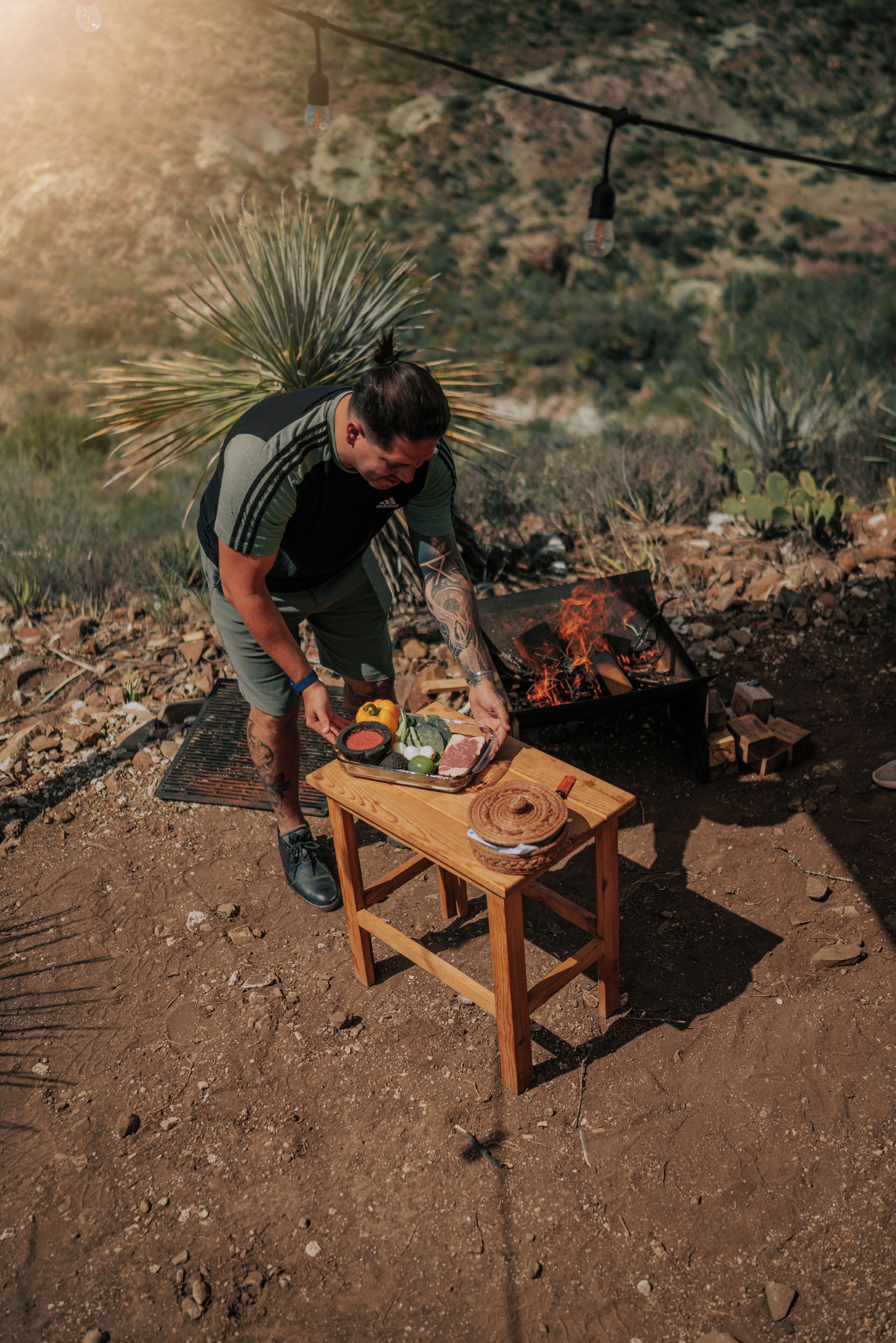 Una persona preparando comida al aire libre, con una parrilla portátil y una mesa de madera.