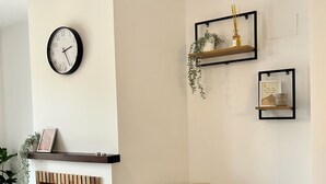 A modern living room with a brick fireplace, a black chair with a beige throw, a wall clock, and two shelves with decorative items. - Hancinda Sleeps 4 With Free Parking (Fuente Alamo de Murcia)