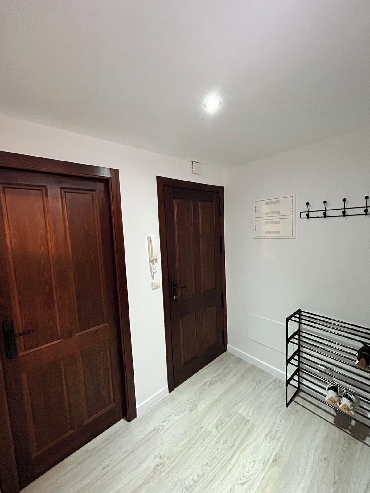 A hallway with wooden doors, a coat rack, and a shoe rack.