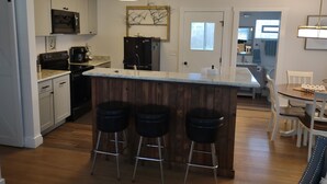 A modern kitchen with a central island, bar stools, and a dining area with a table and chairs.