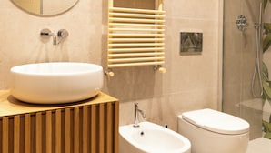 Casa de banho moderna com espelho redondo, lavatório sobrepor, bidé e cabine de duche com vidro.