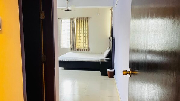 Una habitación con cama, ventilador de techo, ventana con cortinas y puerta.