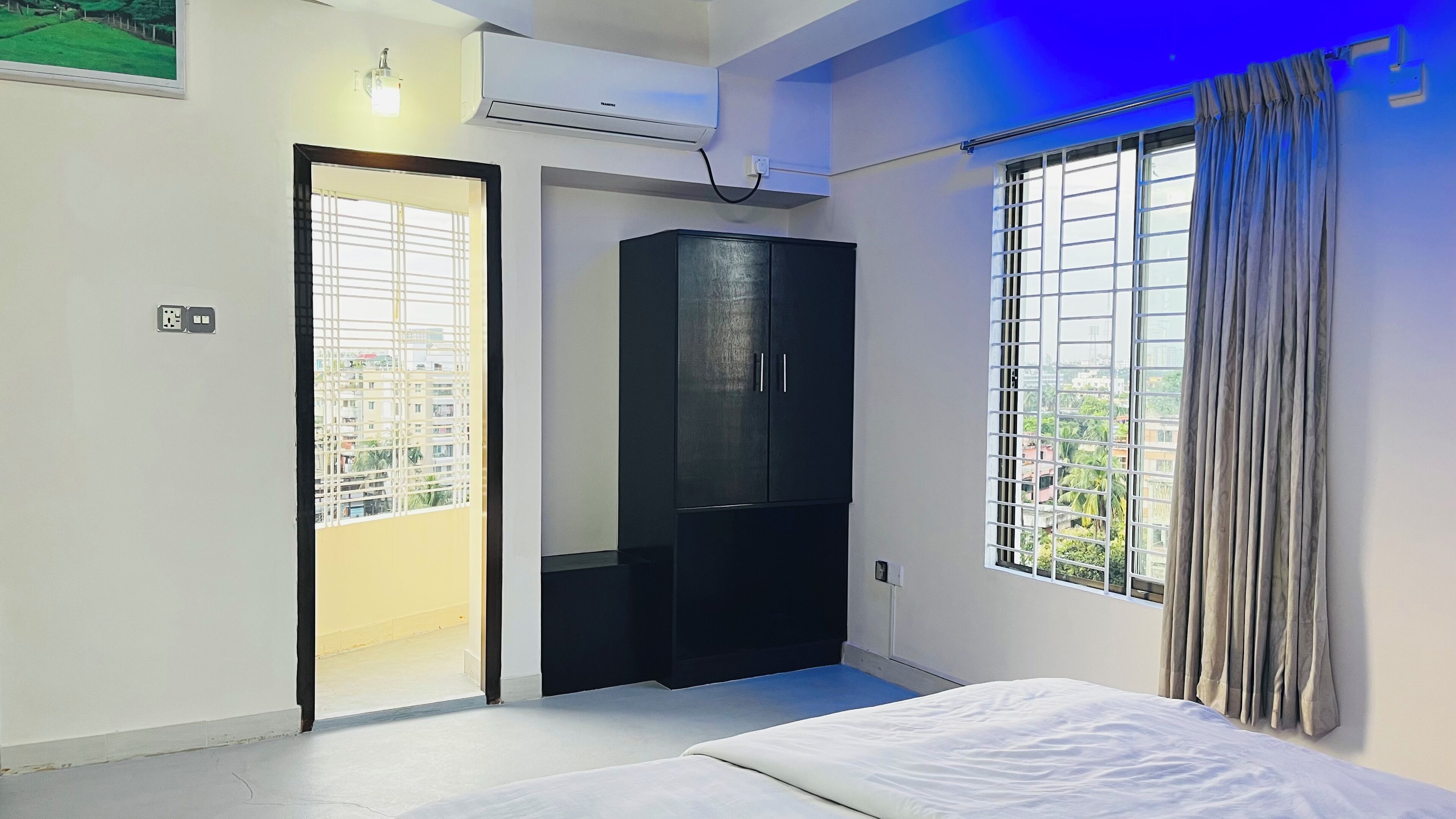 A bedroom with a bed, a wardrobe, a window with curtains, and an air conditioning unit.
