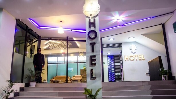 L’entrée d’un hôtel au design moderne, avec une grande enseigne lumineuse, un escalier menant au hall d’entrée et un espace de réception orné d’un logo.