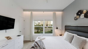 A modern bedroom with a large bed, a flat-screen TV, a dresser, and a window with curtains.