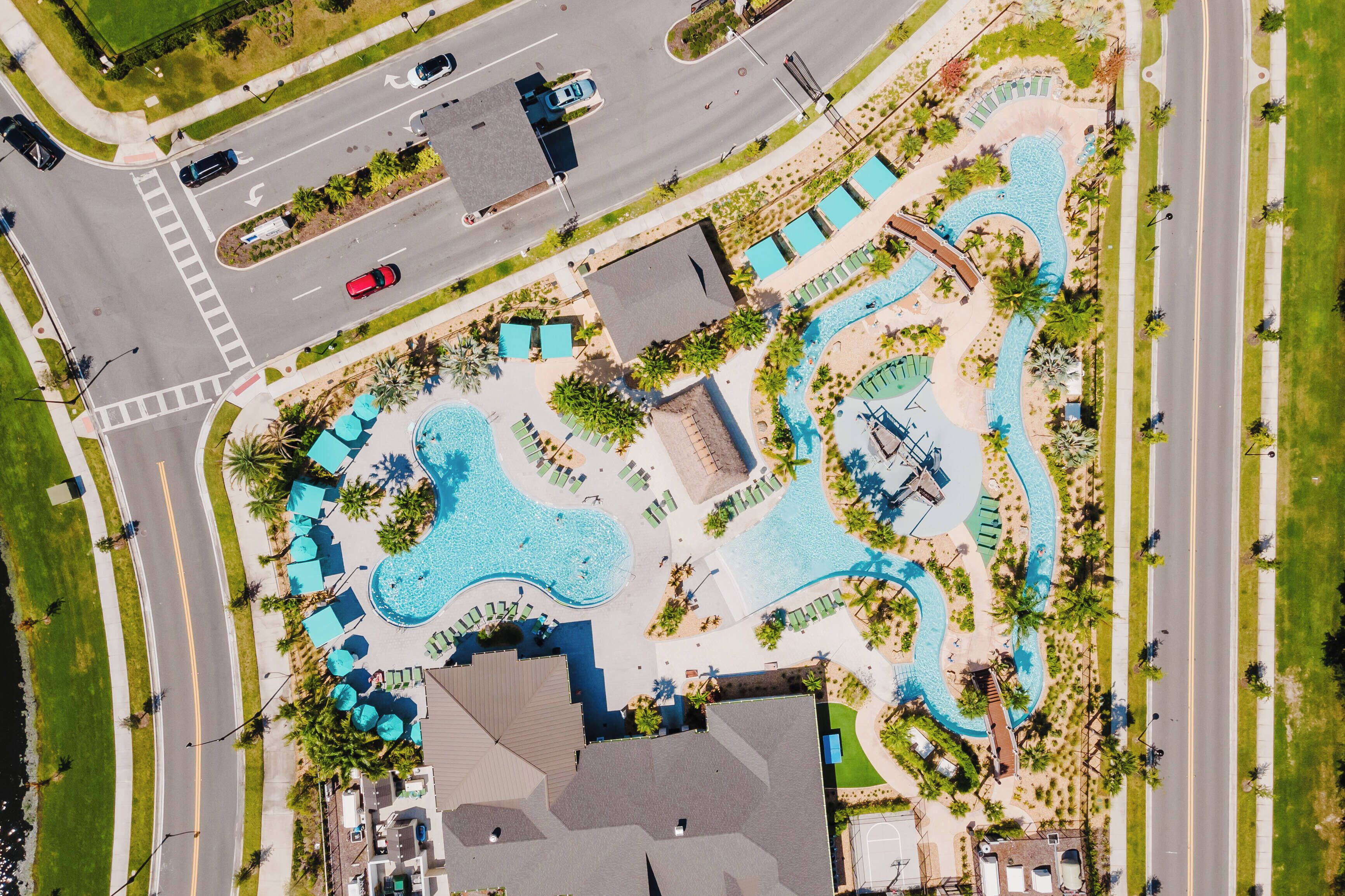 Eine Luftaufnahme eines Resorts mit einem großen Schwimmbecken, mehreren Liegebereichen und einer nahegelegenen Straße.