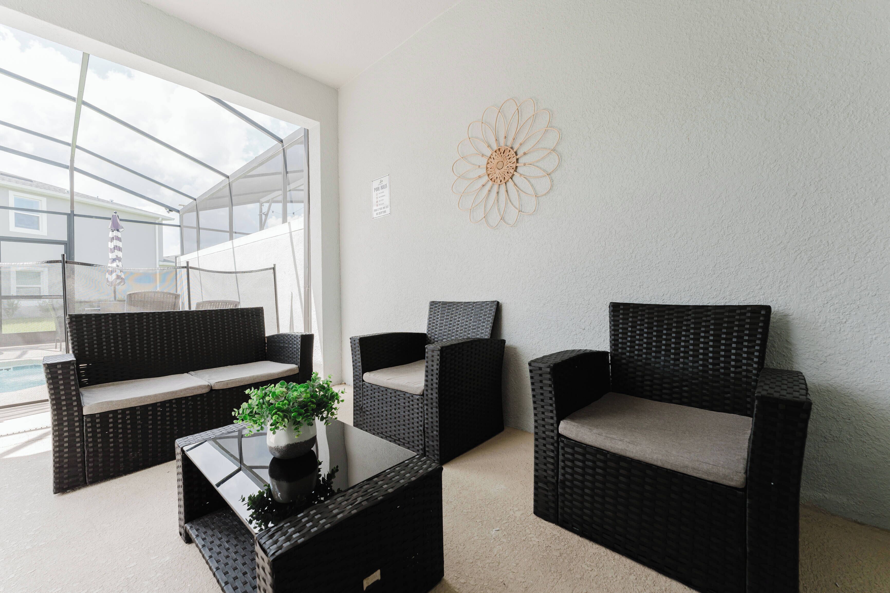 A sunlit patio area with wicker furniture, a glass table, and a decorative wall piece.
