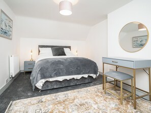 Ein Schlafzimmer mit Bett, Nachttischen, Schreibtisch, Stuhl, rundem Spiegel und Heizkörper.