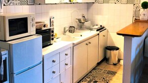 Een kleine keuken met witte kastjes, een magnetron, een spoelbak en een klein afvalbakje.