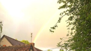 Een huis met een pannendak, een kleine tuin en een zichtbare regenboog.