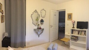 Een woonkamer met een bank, een rode fauteuil, een boekenkast, een televisie en een deur die naar een andere kamer leidt.