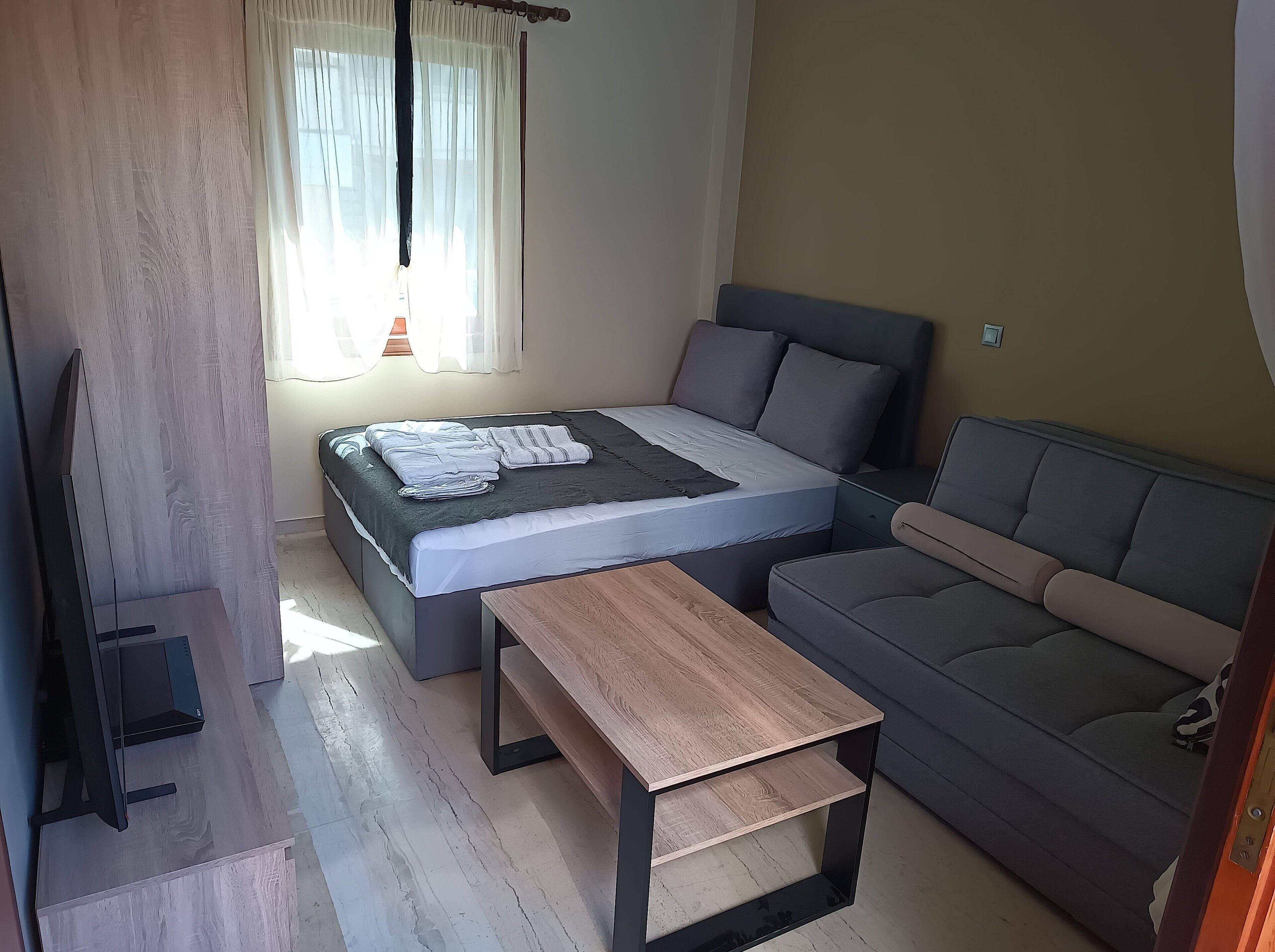 A modern bedroom with a bed, a sofa, a wooden table, and a TV.