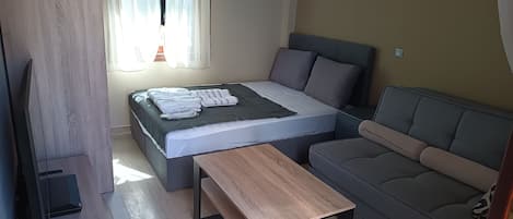 Une chambre à coucher moderne avec un lit, un canapé, une table en bois et un téléviseur.