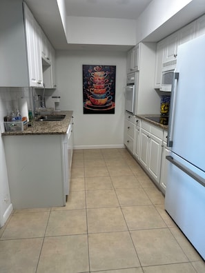 A modern kitchen with white cabinets, a stainless steel refrigerator, and a tiled floor. - Seaside Bliss 2BR Beach Condo (Satellite Beach)