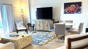 Een woonkamer met een flatscreen televisie, een bank, een eettafel en een kamerkleed met een patroon.