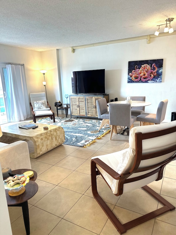 A living room with a flat-screen TV, a sofa, a dining table, and a patterned rug. - Seaside Bliss 2BR Beach Condo (Satellite Beach)