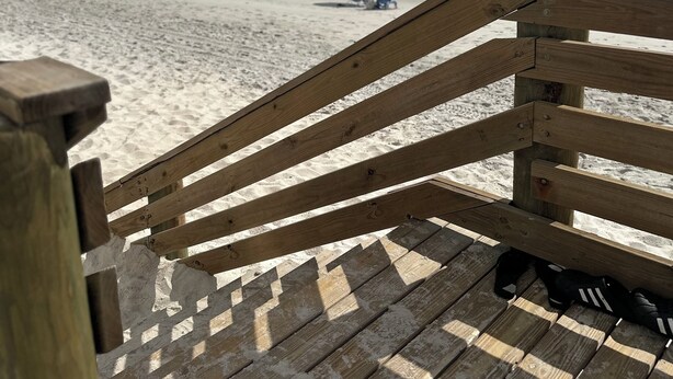 Een houten terras dat uitkomt op een zandstrand, met een heldere lucht.