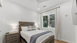 Ein Schlafzimmer mit einem hölzernen Bett, Nachttischen, einem fenster mit Vorhängen und einem Deckenventilator.
