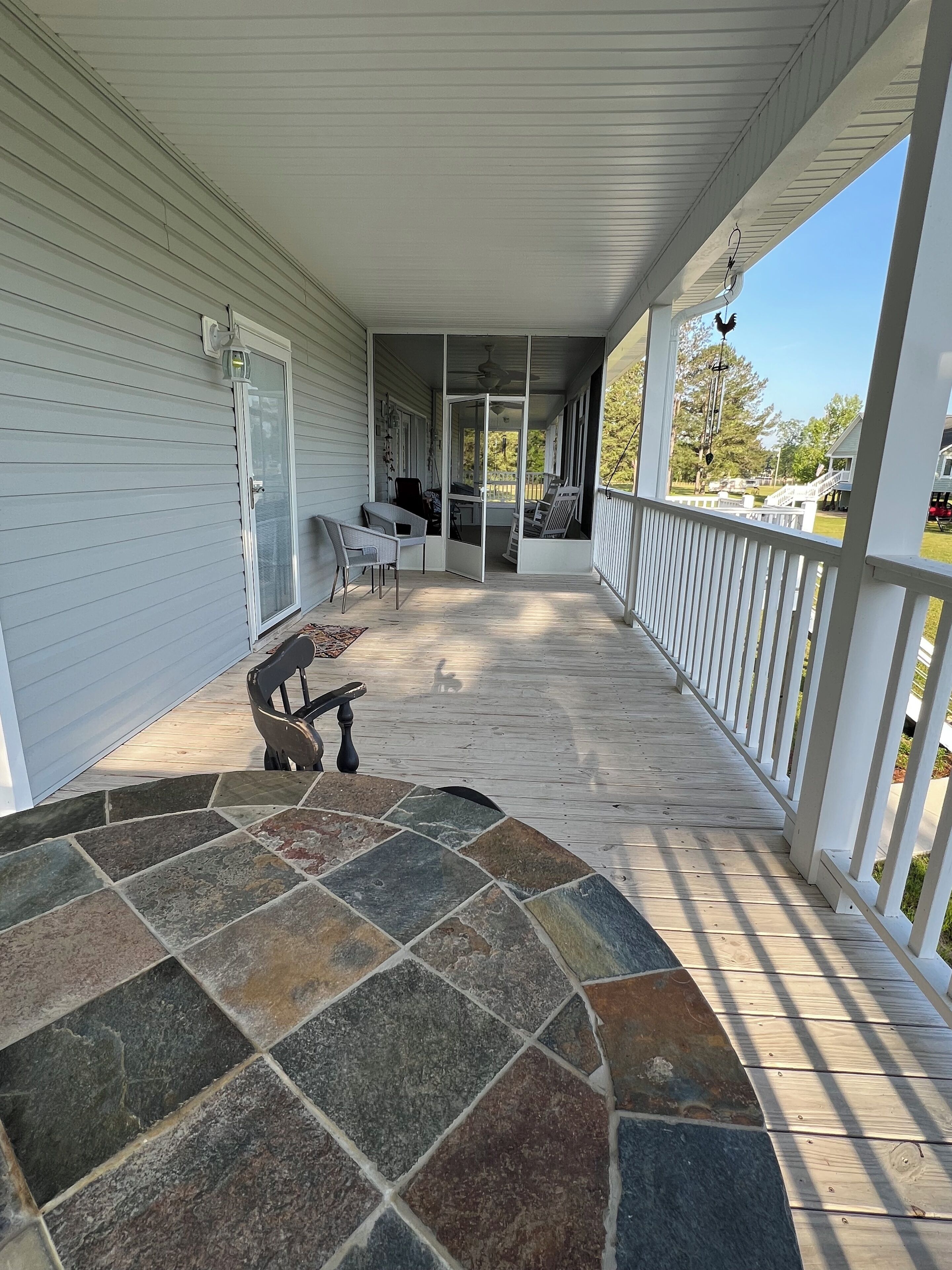 A covered porch with a stone-tiled entrance, white railings, and a view of the yard.